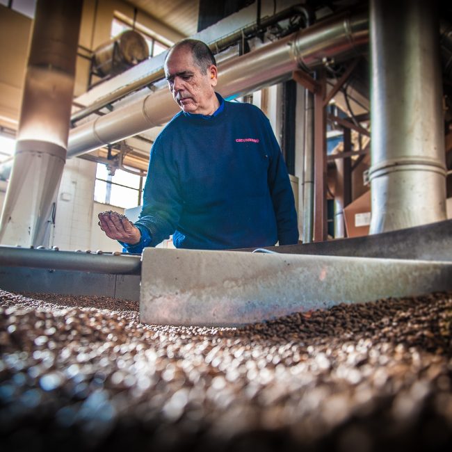 Detalle de trabajador cogiendo granos de café en un molino.